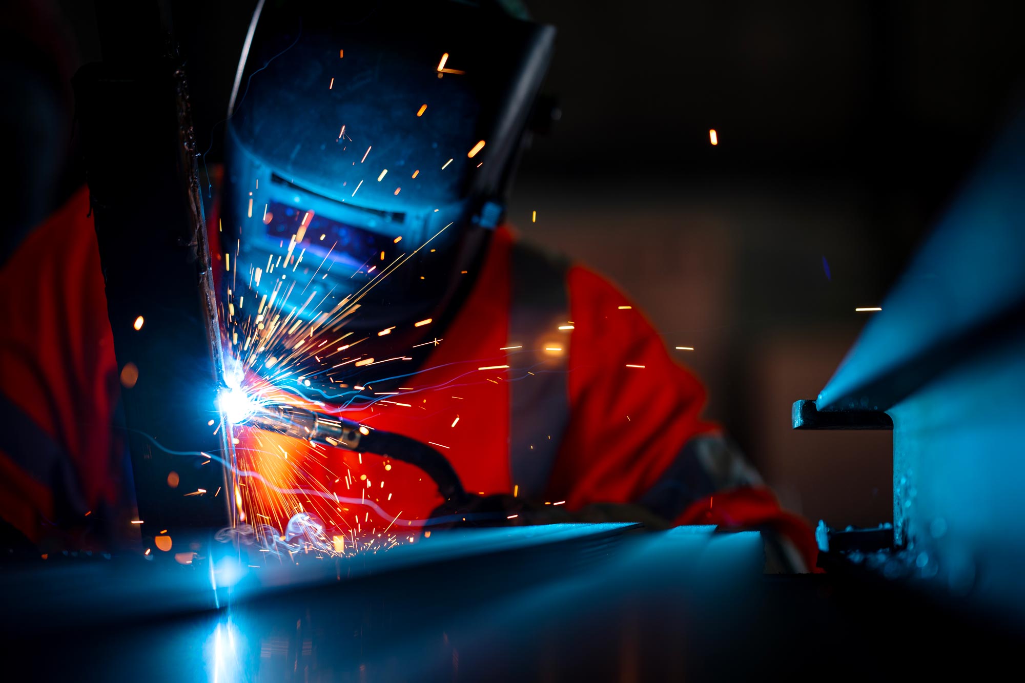 Närbild på svetsare som arbetar på metall med flygande gnistor